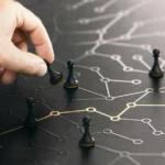 Dłoń umieszczająca pionka w złożonej, ciemnej sieci połączonych punktów danych i relacji, stanowiąca metaforę ujednoliconego profilu klienta i platformy Customer Data Platform.